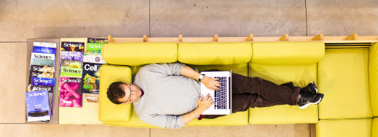man laying on a yellow couch typing on a laptop